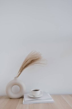 Fluffy pampas grass / straed in stylish vazo, kahve fincanı ve dergiler beyaz duvara karşı. Minimum iç dekorasyon. Blogcular için modaya uygun bir kavram. Paris titreşimleri.