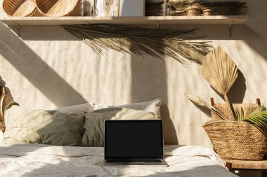 Boş ekran laptop. Duvarda sıcak güneş ışığı gölgeleri. Paris havası. Sıcak bohem tarzı ev dekorasyonu. Uzay modelleme şablonunu kopyala. Yatak odası, yastık, çarşaf, dekorasyon..