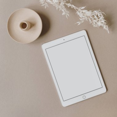 Boş ekran tableti. Tarafsız pastel bej arka planda beyaz çiçek dalı. Düzlük, üst görünüm minimalist yaşam tarzı blogu, web sitesi şablonu. Boşluk modellemesini kopyala.