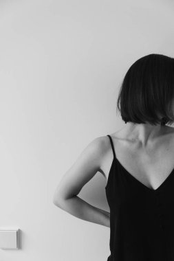 Beyaz duvara yaslanmış genç ve güzel bir kadın. Monokrom moda minimalist kavram.