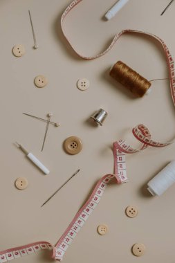 Dikiş aletleri: düğmeler, makara, yüksük, bej arka planda mezura. Düz yerde, üst tarafta. Hobi, eğlence konsepti.