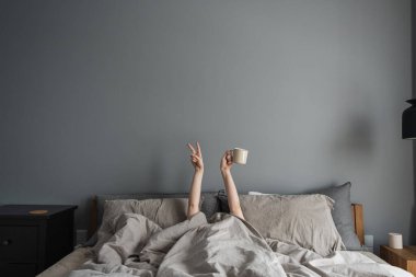 Kadın, elinde kahveyle elinde fincanla yatakta uzanıyor ve 