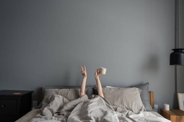 Kadın yatakta uzanıyor ve elinde kahveyle fincanı tutuyor ve 