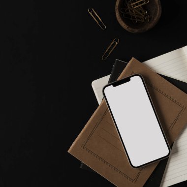 Boş ekran, cep telefonu, defterler, siyah arka planda tahta kasede klipler. Ofis masası çalışma alanı. İş, iş planı. Düz yatış, üst görünüm.