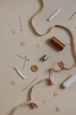 Dikiş araçları: düğmeler, makara, yüksük, mezura, tarafsız bej arka planda iğneler.