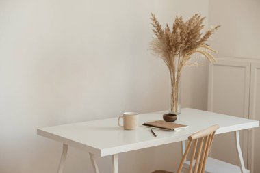 Estetik düşük ofis çalışma alanı iç tasarımı. Kupa, defter, pampa, çiçek buketi beyaz masada beyaz duvara karşı. Kız ve kadın patron ev işi konseptinde çalışıyor..