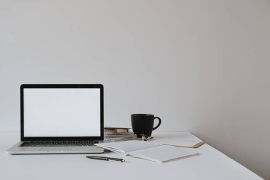 Boş fotokopi odası olan dizüstü bilgisayar kahve fincanı ile masada, beyaz duvara karşı kağıt çarşaf. Minimalist ev ofis çalışma alanı.