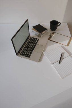 Minimalist ofis masası çalışma alanı. Masada kahve fincanı, kağıt çarşaf ve beyaz duvarda kırtasiye malzemesi olan dizüstü bilgisayar. İş, iş geçmişi.