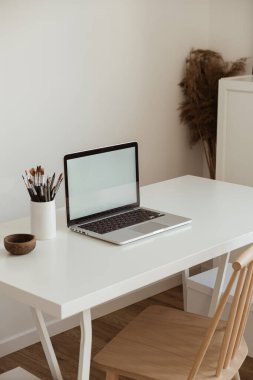 Masanın üzerinde beyaz duvara karşı kırtasiye malzemesi olan boş bir ekran olan dizüstü bilgisayar. Minimalist ev ofis çalışma alanı. Model şablonu.