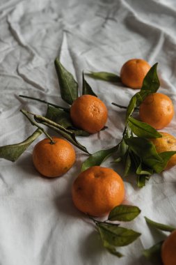 Çiğ portakal, yeşil yapraklı mandalina ve buruşuk keten kumaş. Sağlıklı gıda konsepti.