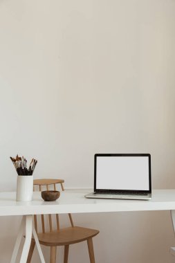 Masanın üzerinde beyaz duvara karşı kırtasiye malzemesi olan boş bir ekran olan dizüstü bilgisayar. Minimalist ev ofis çalışma alanı. Model şablonu.