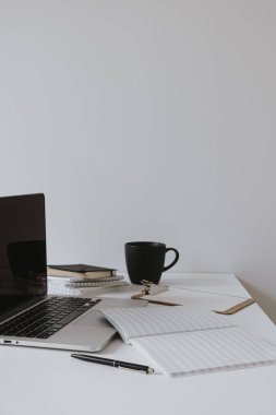 Minimalist ofis masası çalışma alanı. Masada kahve fincanı, kağıt çarşaf ve beyaz duvarda kırtasiye malzemesi olan dizüstü bilgisayar. İş, iş geçmişi.