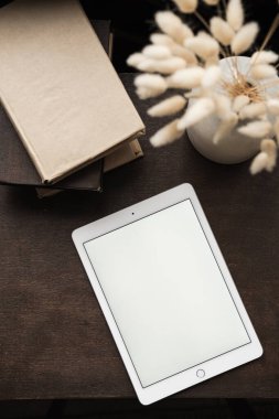 Boş tablet tableti, kitaplar, derin kahverengi arka planda tavşan kuyruğu çimen buketi. Blog, sosyal medya, web, dergi fotokopi uzay şablonu. Düz yatış, üst görünüm.