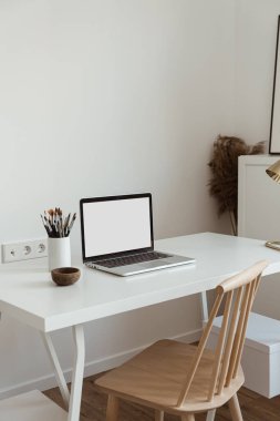 Masanın üzerinde beyaz duvara karşı kırtasiye malzemesi olan boş bir ekran olan dizüstü bilgisayar. Minimalist ev ofis çalışma alanı. Model şablonu.