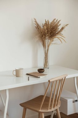 Kadınlar için ev ofis çalışma alanı. Serbest çalışma, iş yeri. Hafif estetik higge alanı, ahşap sandalye, masa, sazlık pampa çim buketi, kupa, defter. Modern iç tasarım.