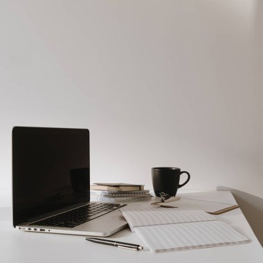 Masada kahve fincanı olan dizüstü bilgisayar, beyaz duvara karşı kağıt çarşaf. Minimalist ev ofis çalışma alanı.