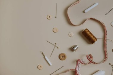 Dikiş araçları: düğmeler, makara, yüksük, mezura, tarafsız bej arka planda iğneler.