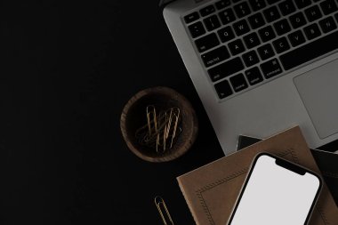 Boş ekran cep telefonu, dizüstü bilgisayar, defter, siyah arka planda kırtasiye malzemesi. Düzlük, üst görünüm minimalist estetik yaşam tarzı blogu, web, sosyal medya şablonu. Boşluk modellemesini kopyala.