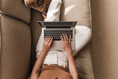Dizüstü bilgisayarda çalışan genç bir kadın kanepede yatıyor. Evde karantinada çalışmak, serbest meslek anlayışı. Kız patron, bayan patron iş kompozisyonu blog, web, sosyal medya