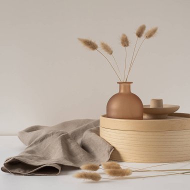 Güzel bronz vazoda tavşan kuyruğu otu, ahşap depolama kutusu, beyaz duvara karşı nötr bej battaniye. Estetik minimal iç tasarım konsepti