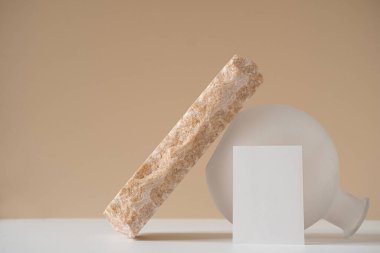 Boş kağıt levha, gül mermer taş, nötr bej duvar karşısında beyaz vazo ile yaratıcı asgari estetik konsept. İşletme markalaşması, blog, sosyal medya şablonu. Boşluk modellemesini kopyala