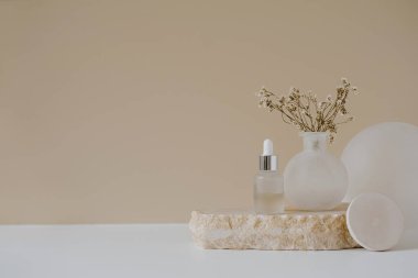 Estetik minimalist güzellik terapisi konsepti. Organik serum yağı kozmetik şişesi. Tarafsız bej arka planda çiçekler var. Vücut derisi, yüz tedavisi ürün bileşimi