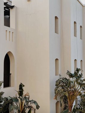 Bej evin yanında yemyeşil yaprakları olan tropik bitki ağaçları, tatil köyü binaları. Seyahat, yaz tatili konsepti