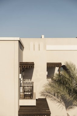 Bej duvarları, pencereleri, güneş ışığı gölgeleri ve tropikal palmiyeleri olan modern doğu tarzı bir bina. Estetik asgari mimari ön cephe tasarım kavramı arka planı