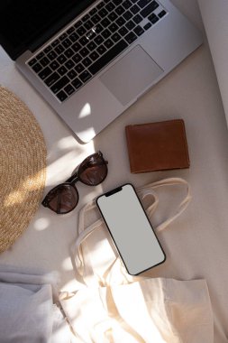 Boş maket ekranlı düz bir cep telefonu. Bulanık güneş ışığı gölgelerinde güzel kadın aksesuarları. Estetik yaşam tarzı moda etkileyicisi blog, dergi, sosyal medya