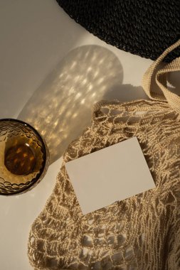 Fotokopi alanı olan boş kağıt kağıdı. Minimum lüks, estetik, marka şablonu. Güneş ışığı gölgeli cam, kadın şapkası, bej arka planda ip torbası. Düz yatış, üst görünüm