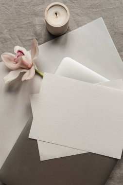 Sahte kopya alanı, dizüstü bilgisayarı, pembe çiçek, tarafsız keten kumaş arka planında mum olan boş kağıt kağıtlar. Asgari estetik iş markası, düğün davetiyesi şablonu. Düz yatış, üst görünüm