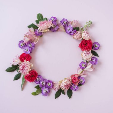 Soyut çiçekli estetik arka plan. Renkli gül çiçeklerinden oluşan yuvarlak çerçeveli çelenk. Pembe arka planda, boş fotokopi alanı modeli var. Güzel çiçekler ve taç yaprakları şablonu