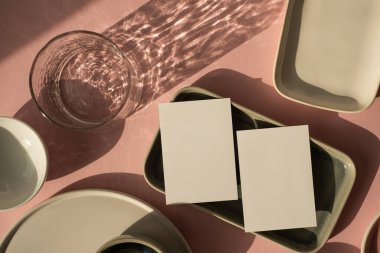 Tozlu pembe arka planda fotokopi alanı olan boş bir kağıt kağıdı. Estetik bohem iş modeli. Seramik tabaklar ve parlak güneş ışığı gölgeli cam.