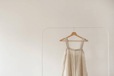 Minimalist gardırop: nötr bej renkli tulum ya da beyaz duvara asılı elbise. Estetik moda konsepti