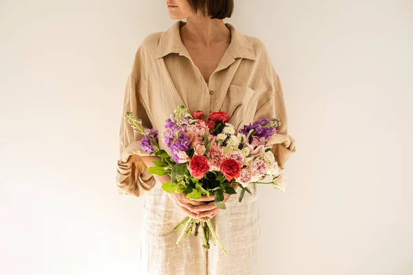 穿着米色麝香衬衫的年轻漂亮的女人拿着一束五彩缤纷的玫瑰花朵贴在白墙上 美丽的节日庆祝花卉创作 — 图库照片