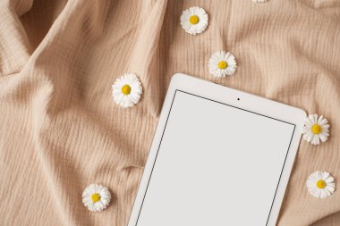 Boş tablet kağıdın düz tableti, papatya çiçeği tomurcukları tarafsız bej muslin kumaş. Estetik kadın, kız patron işi, iş, blog şablonu ve maket alanı. Düz yatış, üst görünüm.