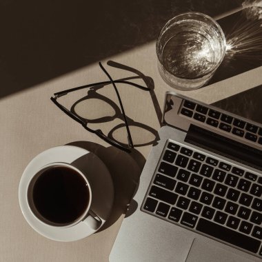 Estetik lüks bohem minimalist ofis çalışma masası. Dizüstü bilgisayar, bir fincan kahve, bardak güneş ışığı gölgeli kristal bardak. Düz yatak, üst görünüm işi, iş konsepti