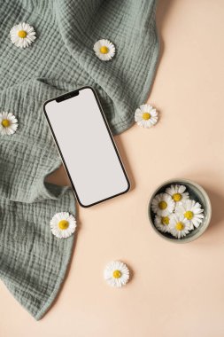 Boş ekran cep telefonu düzlüğü, papatya çiçeği tomurcukları, bej arka planda akuamarin muslin bezi. Estetik sosyal medya, blog şablonu ve maket alanı. Düz yatış, üst görünüm.
