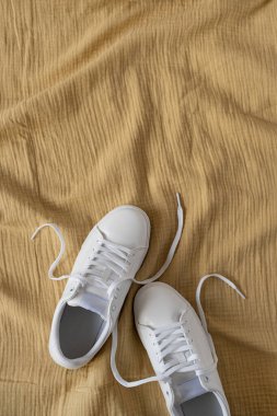 White female sneakers on yellow crumpled muslin cloth background. Flat lay, top view. Merchandise, marketing, sale, shopping concept clipart