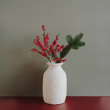 Beyaz vazoda kırmızı böğürtlen ve çam filizi. Sönük yeşil arka planda Noel ve kış iç dekorasyonu