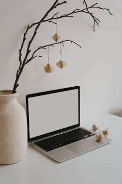 Dizüstü bilgisayarı, organik vazosu, narin asılı fenerleri olan küçük bir masa sahnesi. Tarafsız dekorlu sakin ve modern çalışma alanı