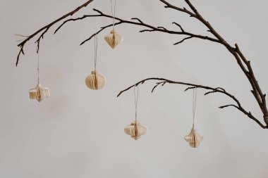 Minimalist dekor. Tarafsız Arkaplan Karşısında Çıplak Dallarda Asılı Zarif Kağıt Süslemeler. Sanatsal Basitlik, İskandinav Tarzı, Çevre dostu Tasarım, İç Estetik