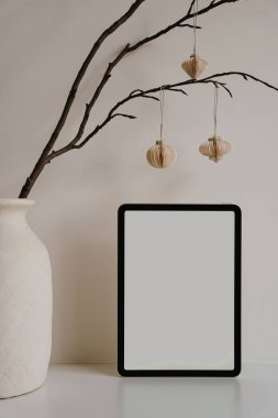 Tablet, kırsal vazo ve kağıt fenerlerle ev ofisinin şık bir düzeni var. Estetik yumuşak nötr tonlar. Sakin yaratıcı alan