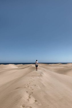 Okyanus kıyısındaki kum tepelerinde yürüyen adam