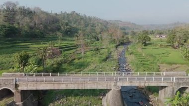 Etrafı yemyeşil pirinç tarlalarıyla çevrili Akan bir akarsu üzerindeki Picturesque Köprüsünün Manzaralı Görünümü