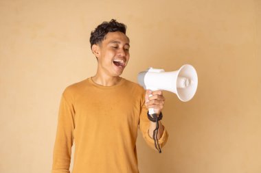 Genç bir adam sevinçle elinde bir megafon tutarak tarafsız bir arkaplanda heyecan sinyali veriyor..