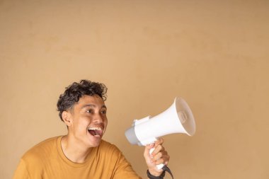 Mesajını basit bir arkaplanda paylaşmak için megafon kullanan genç bir adam..