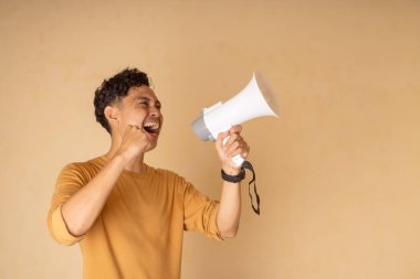 Neşeli bir genç adam tarafsız bir arkaplana karşı megafon kullanıyor..