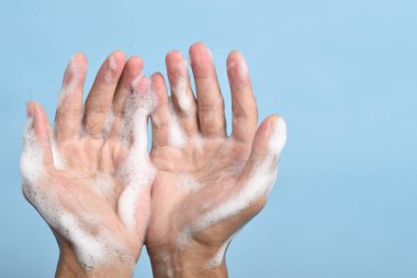 Mavi arka planda düşmüş saç tellerini tutan şampuan köpüğüyle kaplı ellerin yakın çekimi saç kaybını ve hijyen kavramını gösteriyor..