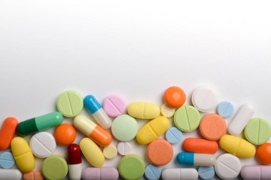 Çeşitli renkli haplar ve kapsüller bir çerçeve oluşturur, beyaz bir arkaplanda izole edilmiş, metin için uzayı kopyalayarak. Tıbbi konsept.